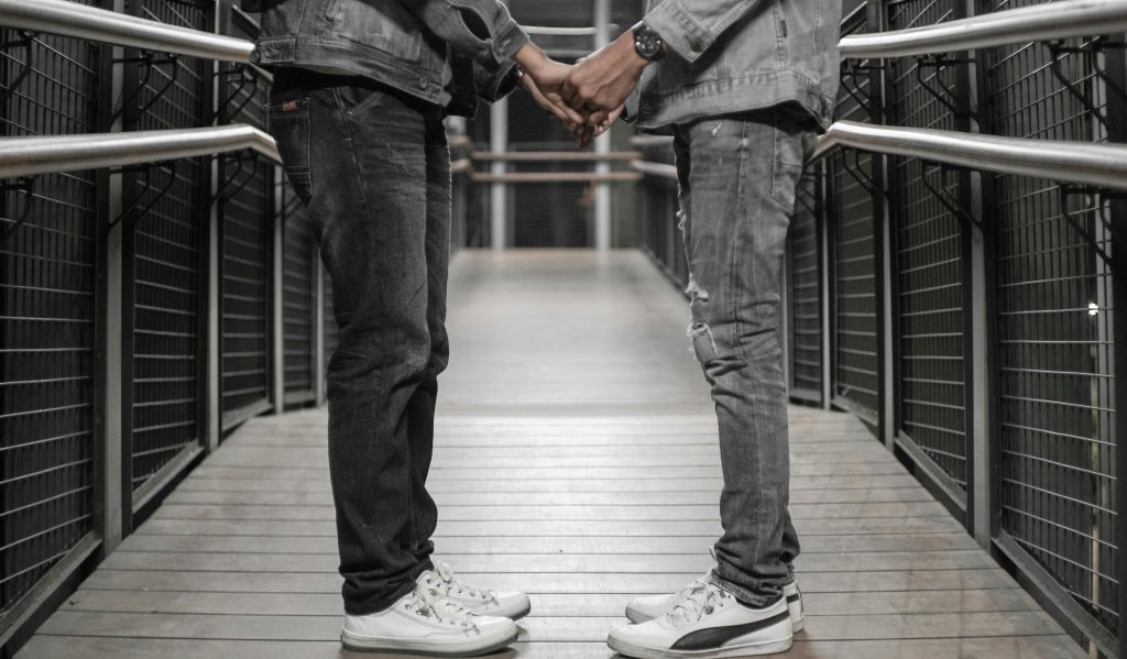 Two adults holding hands on a steel bridge walkway, symbolizing connection.